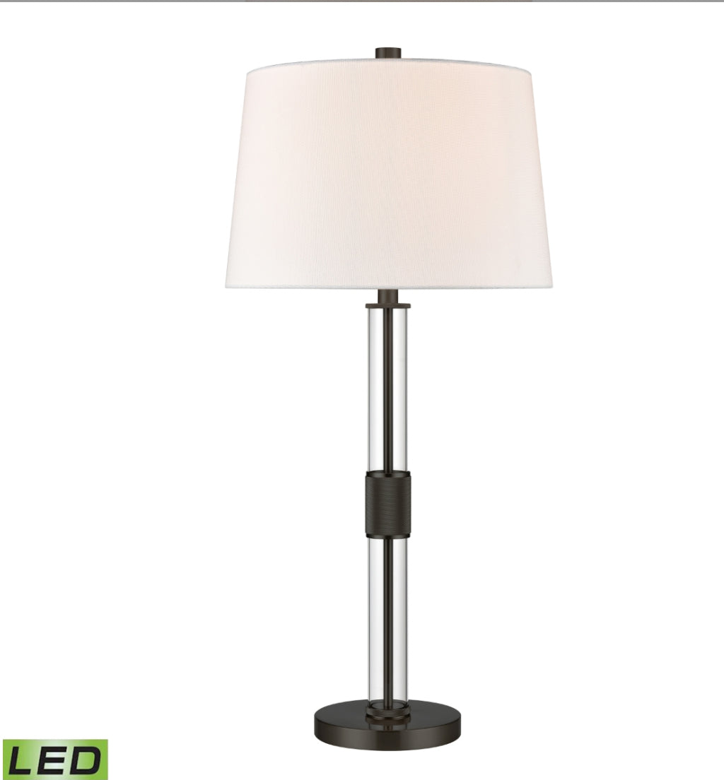The Roseden Court Table Lamp “33” makes a striking addition to a modern, glam style living room, bedroom or hallway. Made from metal in your choice of sleek black or aged brass finishes, its central pole features a knurled texture detail encased in a clear glass tube. This chic design is topped with a round, hardback shade in white linen and is the perfect accent for bringing an elevated touch to a modern interior.