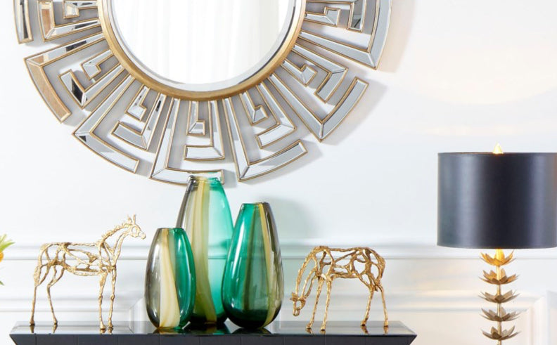 Transform an entryway into an Egyptian-inspired palace with this eye-catching clear and gold mirror. A gorgeous silhouette comprised of a myriad of geometric shapes brings a contemporary feel to spaces, while honoring the classic royal inspiration of the sun.  Dimensions: 47 x Ext 1.5  Finish: White Materials: Ceramic with Off White Linen Shade with White Lining             