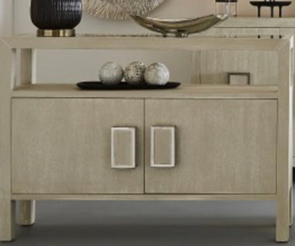 The Hawick Console Table is a striking two-door storage credenza made from ash solids and veneer with a weathered white painted finish.   The top is made from white painted wood veneer, and a lower shelf above the storage doors offers an additional display surface.  Each door features a central metal rectanglular door handle with a center panel made from the same cerused wood.  Dimensions:48" W x 11" D x 34" H