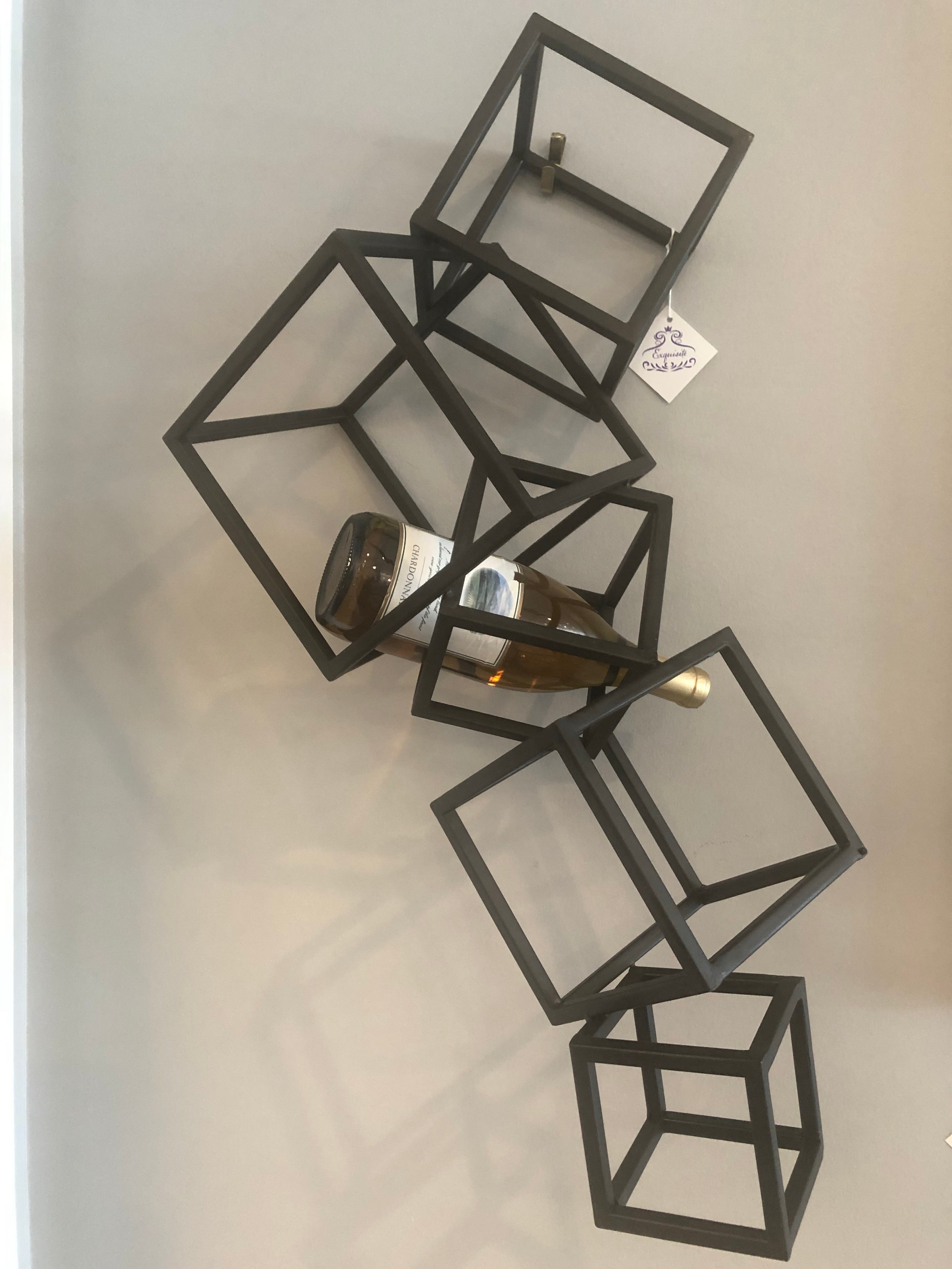 This wall décor features individual metallic squares that are fashioned together. The sizes of the square vary on their positions and are angled outward to give this wall art a 3-D effect. Use to hold your favorite bottle or just simply as wall decoration.  Dimensions: H 11 x W 23.75 x Ext 0.25  Finish: Black Materials: Iron